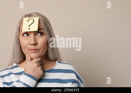 Emotional Mature Woman With Question Mark On Beige Background Stock