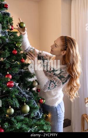 Joyful Woman Hanging Christmas Ornaments On Spruce Tree Outdoors In