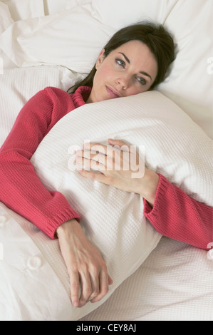 Brunette Female Wearing A Red Cable Knit Jumper Lying In Bed Under A