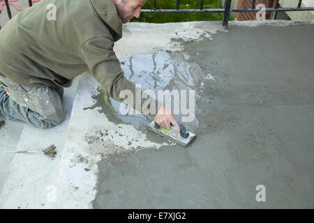 Workman smooths a skim coating of cement on old stairway Stock Photo