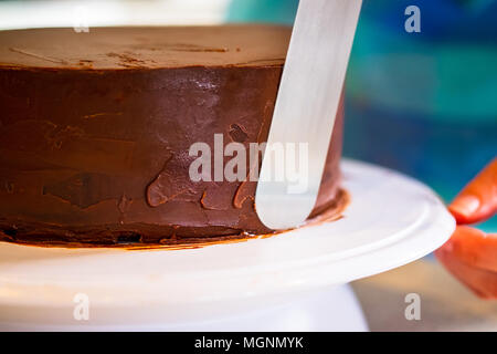 A Woman Applying Chocolate Ganache Icing Or Frosting To A Cake Using A