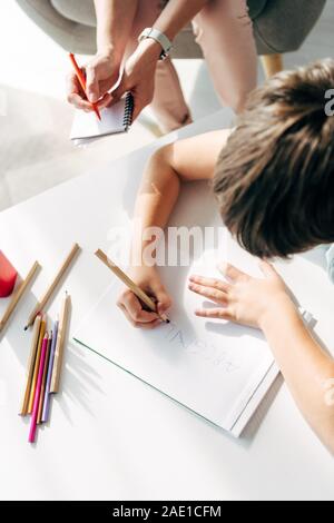 Niño con dislexia dibujo sobre papel con un lápiz y un psicólogo