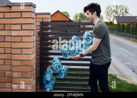 Hombre joven tirando botellas de plástico vacías de agua en el cubo de