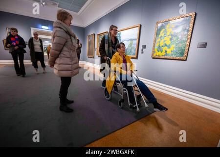 Plusieurs personnes regardent quelques tableaux dans la salle dédiée à