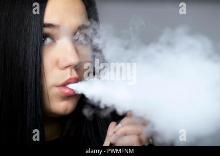 Jeune fille brune vaping nuages de fumée avec vaporisateur populaires