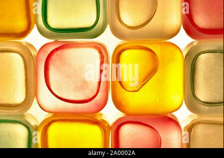 Plastic transparent colored ice cubes arranged in rows with harsh LED back lights resulting in a colorful abstract background.