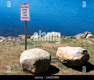 A  white 'please stay off the rocks' sign at a park on Lake Pleasant in Speculator, NY USA in the Adirondack Mountains. Stock Photo