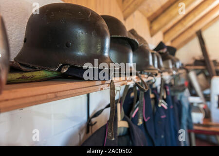 Perspective view along lined up old fire-fighter uniforms with focus on a historical helmet in the foreground. Stock Photo
