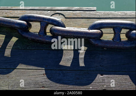 A heavy metal anchor chain lies on a wooden wharf Stock Photo