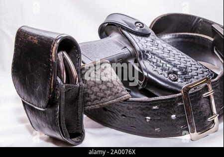 A worn police duty belt with a black pistol and handcuff case wrapped up on a white background Stock Photo