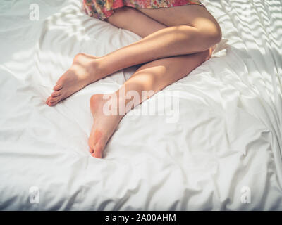 The legs of a young woman lying in bed on a sunny day Stock Photo