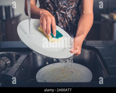 A young woman is cleaning the dishes by the sink in her modern kitchen Stock Photo