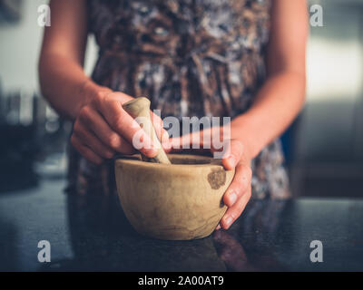 A young woman is using a pestle and mortar in her kitchen Stock Photo