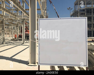 Object under construction stand at the construction site. Blank display board against prefabricated multi-storey building at the background