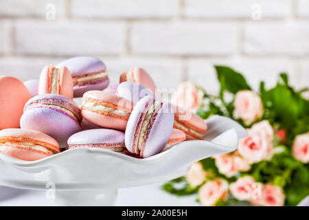 close-up of macarons on a white platter. beautiful bouquet of roses and brick wall at the background Stock Photo