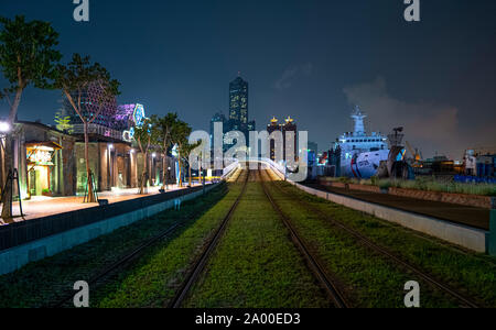 Kaohsiung, Taiwan: View of the green gras covered Kaohsiung Light Rail train tracks leading toward the Tuntex Sky Tower 85 in City Center at night. Stock Photo