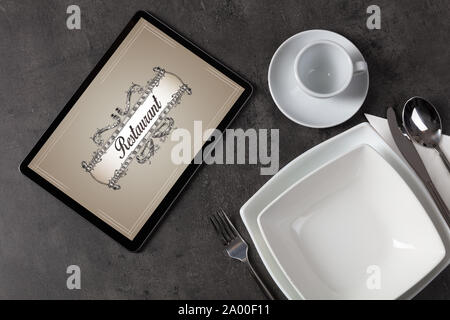 Tablet with stylish restaurant logo and laid table Stock Photo