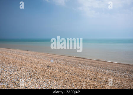 Lone gull flying over shingle on the pebbly beach at Dungeness in Kent, UK Stock Photo
