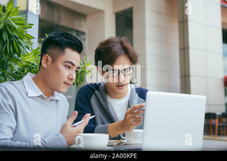 Two young businessmen are chatting in a coffee shop. - Image Stock Photo