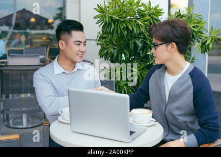 Two young businessmen are chatting in a coffee shop. - Image Stock Photo