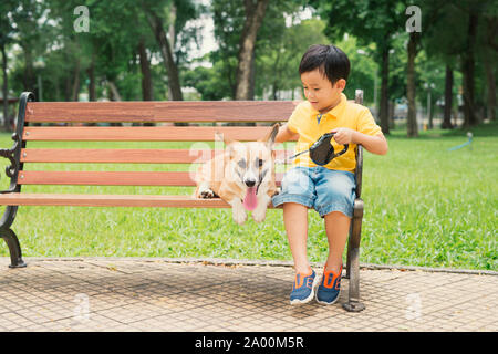 Children and dogs outdoors. Asian little boy enjoying and playing in park with his adorable Pembroke Welsh Corgi. Stock Photo