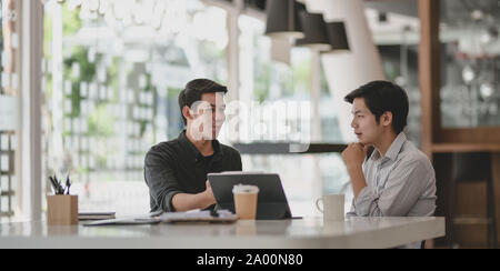 Two professional businessmen discussing their progress of their current project while using tablet Stock Photo