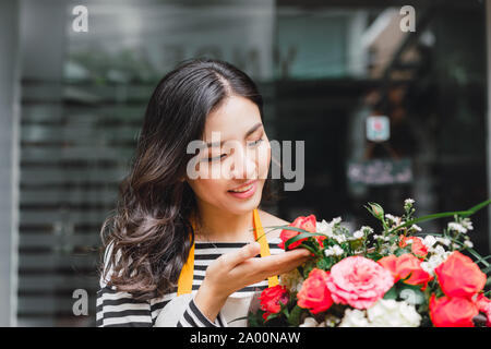 Smiling woman florist, small business flower shop owner, at counter, looking friendly at camera working at a special flower arrangement. Stock Photo