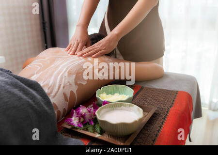 Spa therapist applying scrub salt and cream on young woman back at salon spa. Hands massaging female back with scrub. Stock Photo