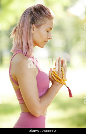 Side view of young blonde girl standing with her eyes closed and concentrating on her relaxation during yoga outdoors Stock Photo