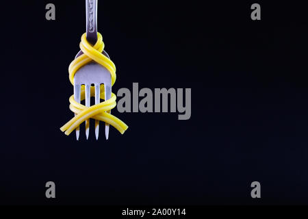 Freshly cooked pasta on a old fork on the black background. Symmetrical loop of spaghetti on an old fork. Stock Photo