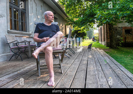 Elderly man sitting on wooden deck of farmhouse in Pinnow, Uckermark,Brandenburg, Germany Stock Photo