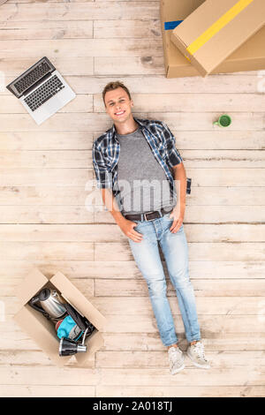 Young man lying on floor surrounded by boxes and laptop smiling cheerful top view Stock Photo