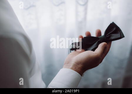 Horizontal image of dark butterfly tie in the hands of a man. Wedding details. Stock Photo
