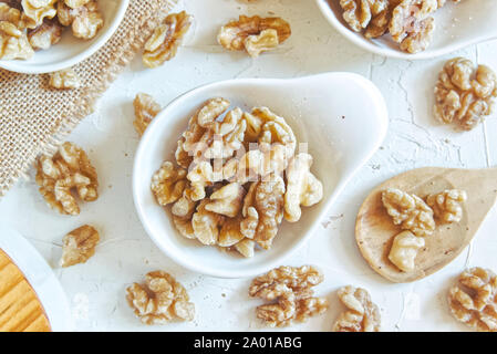 Natural brown walnuts in bowls on a white wooden table of a rustic kitchen. Sackcloth and wood spoon with empty copy space for Editor's text. Stock Photo