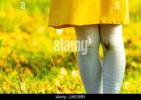 Dirty knees, baby. Little girl in a yellow dress and white stockings after falling to the ground. Stains of dirt on your knees. Autumn day Stock Photo