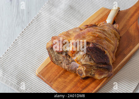 Roasted leg of lamb resting on a wooden chopping board and place mat.  Grey wood background Stock Photo