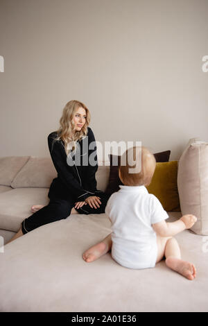 Young blonde mother having quality time with her baby boy son at family home flat - Wearing black budoir dress costume sleeping gown Stock Photo