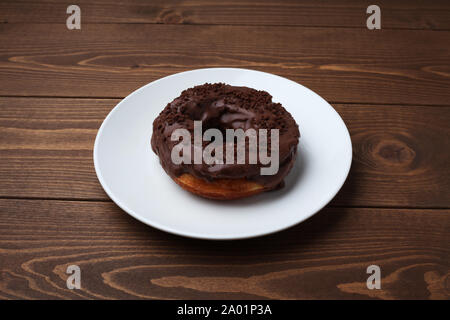 chocolate frosted doughnut on plate isolated on wooden table Stock Photo