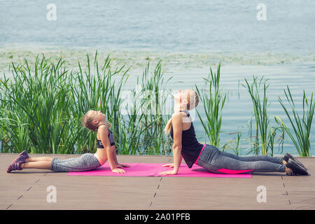 woman and child are training near the lake on a pier, sporty mother and daughter, fitness, yoga Stock Photo