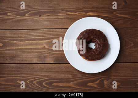 chocolate frosted doughnut on plate isolated on wooden table Stock Photo