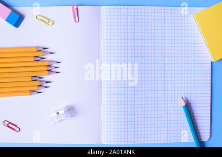 Notebook in a cage with a pencil, eraser, ruler, paper clips and other office supplies on a blue background. Concept back to school. Place for text. Stock Photo