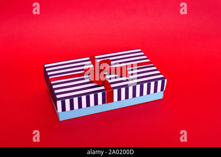 Gift striped box with a red satin bow on the red background. Stock Photo