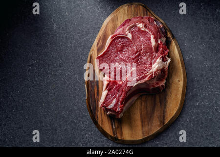 Raw beef steak and cutting board on dark stone background. Top view Stock Photo