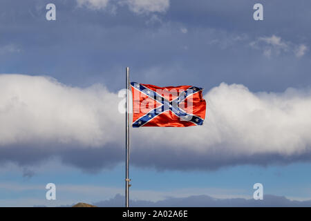 Confederate flag flutters on the wind against white clouds Stock Photo