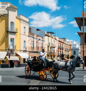Seville, Spain - Sept 10, 2019: Old horse drawn carriage carrying tourist passengers with vibrant Spanish architecture in background Stock Photo