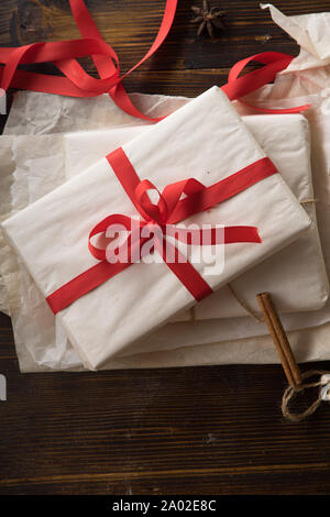 Preparation of christmas gifts. Present covered in white paper with red ribbon. Overhead view. Stock Photo