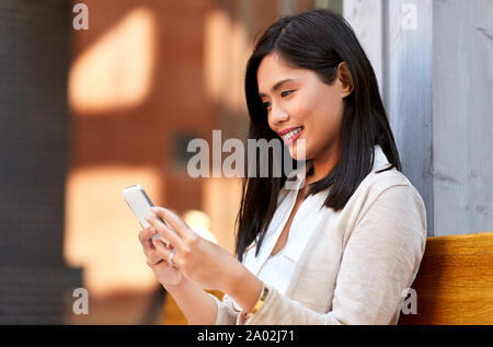 asian woman using smartphone sitting on bench Stock Photo