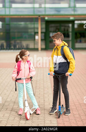 happy school children with backpacks and scooters Stock Photo