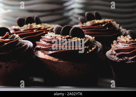 Dark Chocolate muffins topped with chocolate frosting, close up, sucked plates in the background