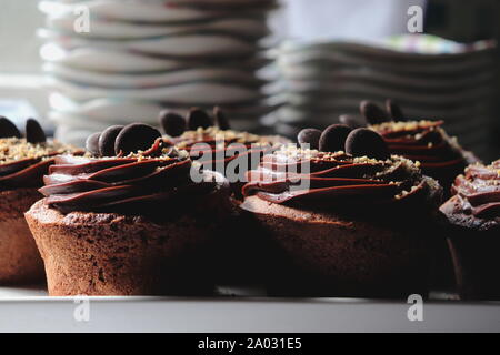 Dark Chocolate muffins topped with chocolate frosting, close up, sucked plates in the background